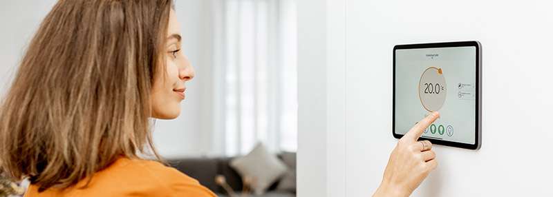 Frau mit kurzen Haaren bedient ein digitales Display zur Temperaturregelung in einem modernen Raum.