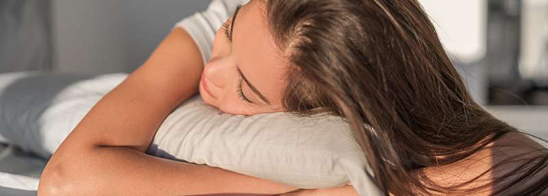 Eine Person liegt entspannt auf einem Kissen und ruht den Kopf auf den Armen in einem hellen Raum.