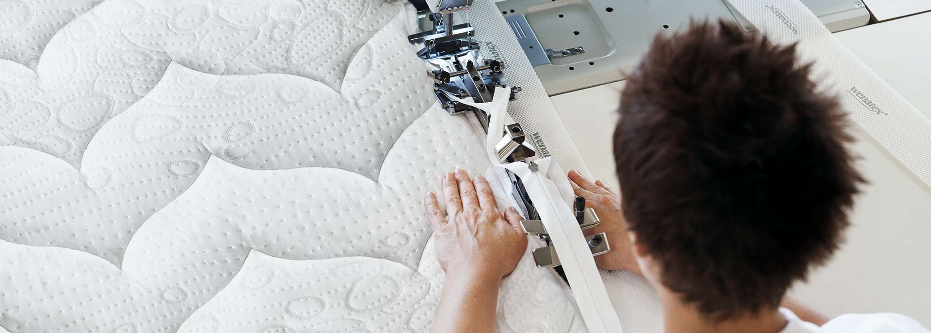 Eine Person näht an einer Matratze mit einer Nähmaschine, die spezielle Stoffe verarbeitet.