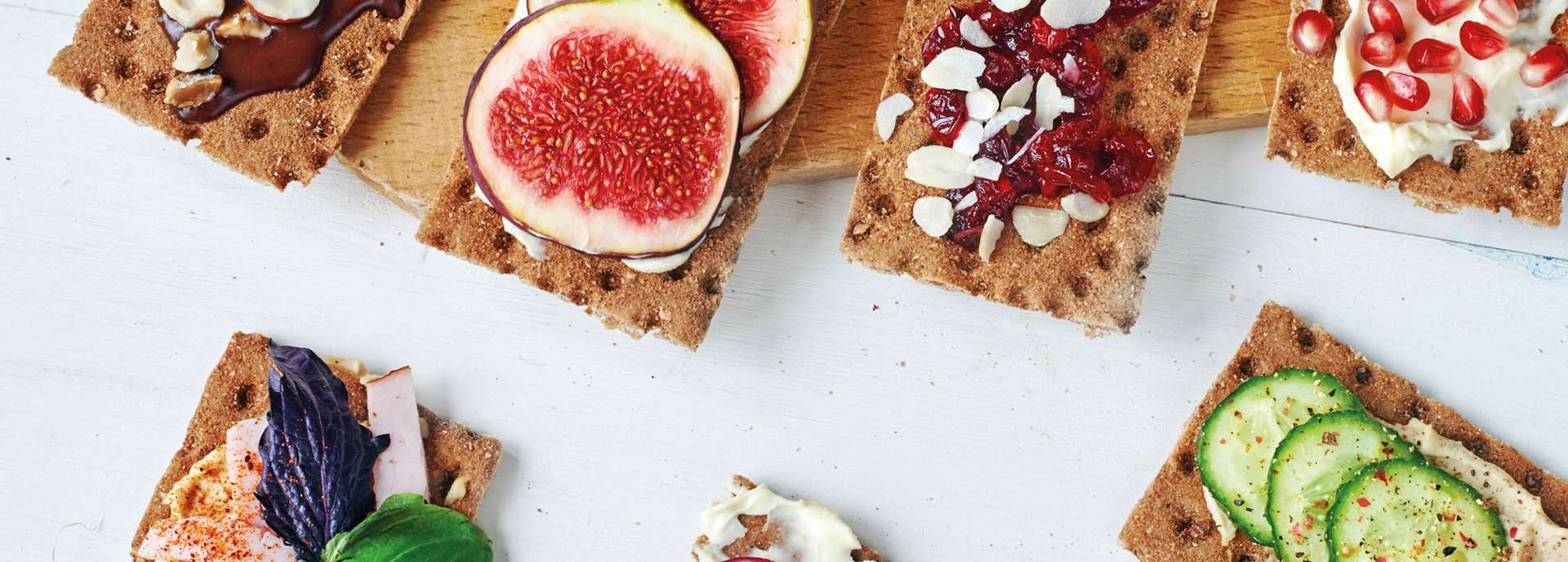 Vielfalt an belegten Knäckebroten mit verschiedenen Toppings wie Obst, Nüssen und Gemüse auf einem Holzbrett.