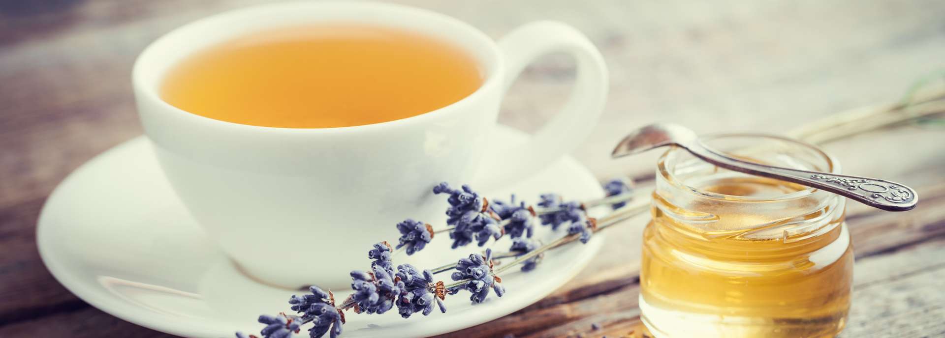 Tasse mit Kräutertee, Lavendelblüten und Honigglas auf einem Holztisch.