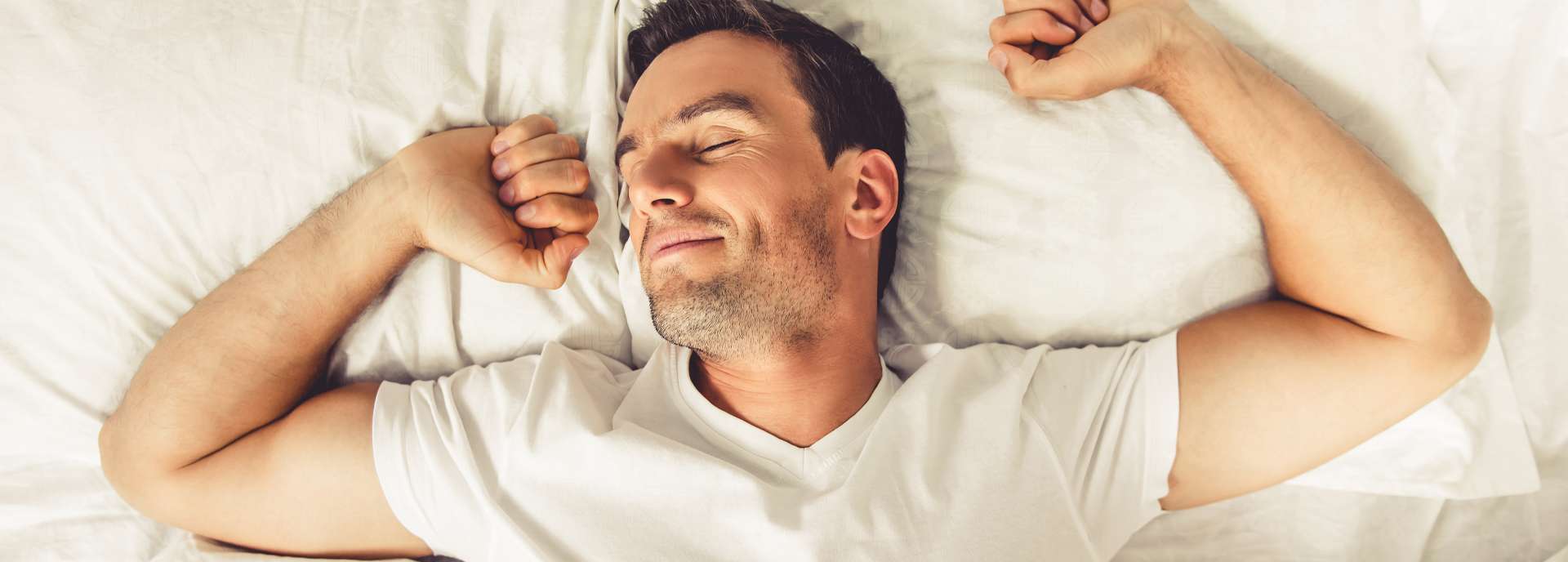 Mann liegt entspannt im Bett und genießt einen erholsamen Schlaf mit einem zufriedenen Gesichtsausdruck.