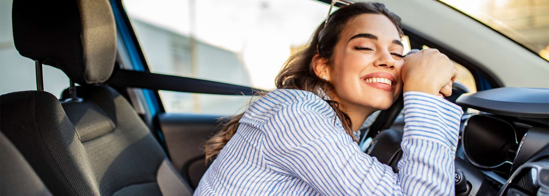 Frau mit lächelndem Gesicht lehnt sich entspannt auf das Lenkrad eines Autos.