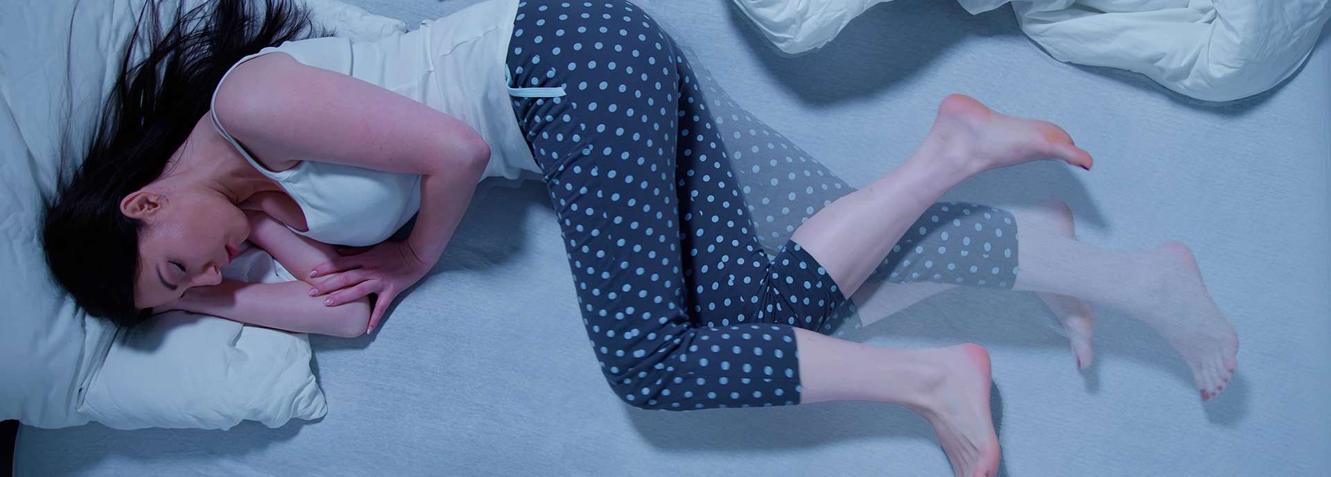 Frau liegt schlafend auf einem Bett, umgeben von Kissen und Decken, in gepunkteter Schlafhose.