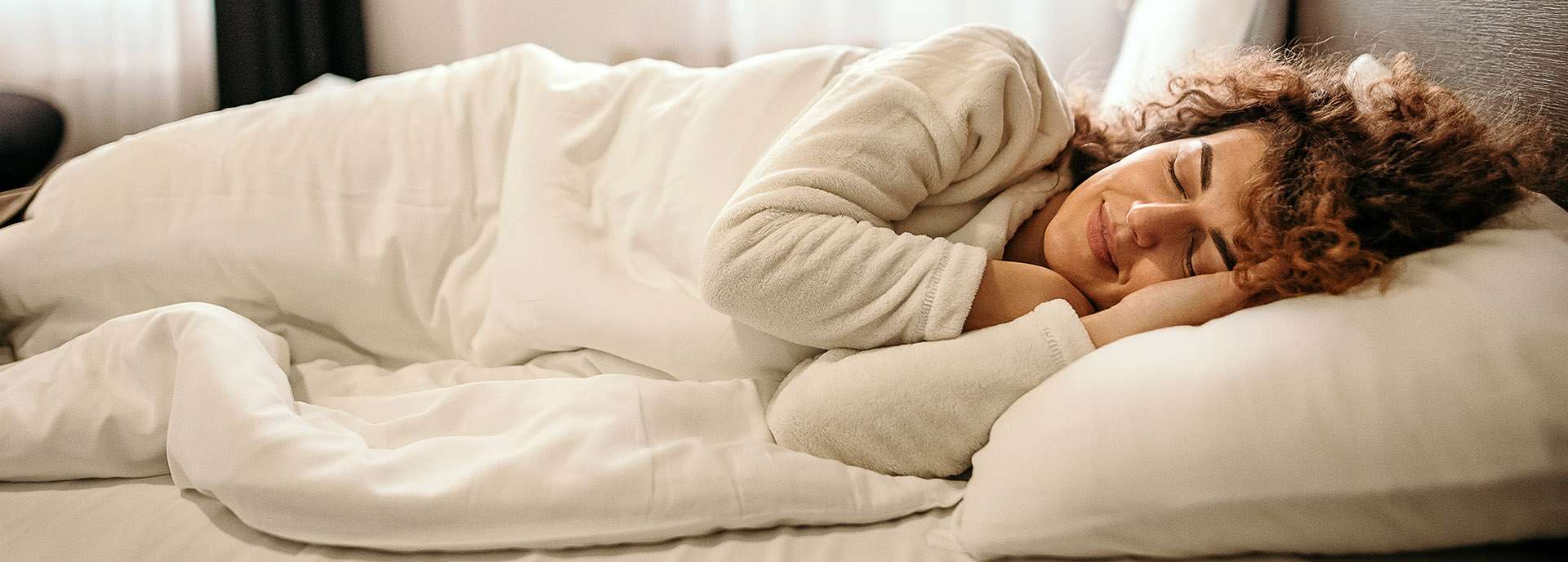 Eine schlafende Frau liegt auf einem Bett, umgeben von weißen Bettdecken und Kissen.