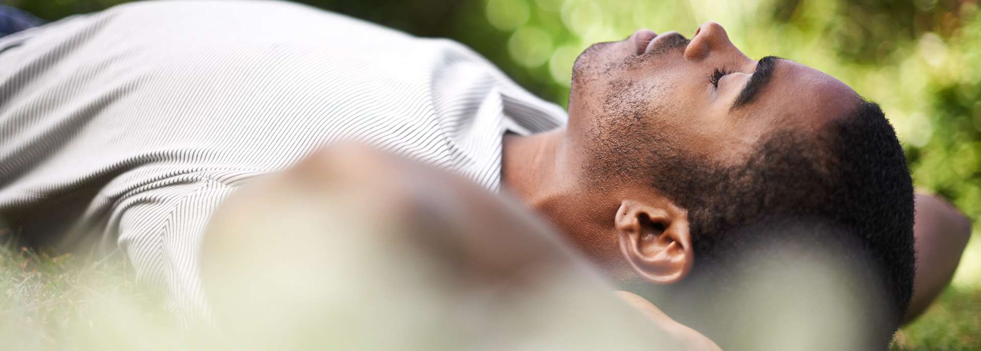 Mann liegt entspannt auf dem Rasen und genießt die Natur, mit geschlossenen Augen und ruhigem Gesichtsausdruck.