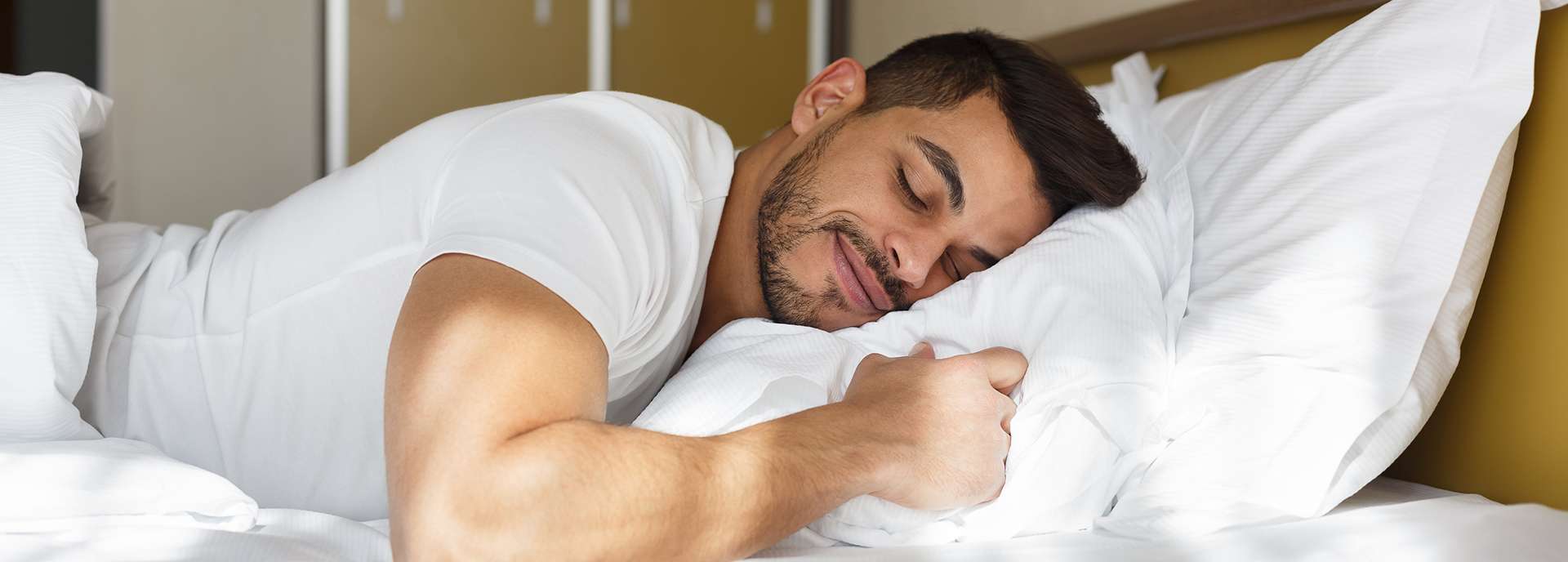 Mann schläft entspannt auf einem Kopfkissen in einem hellen Schlafzimmer.