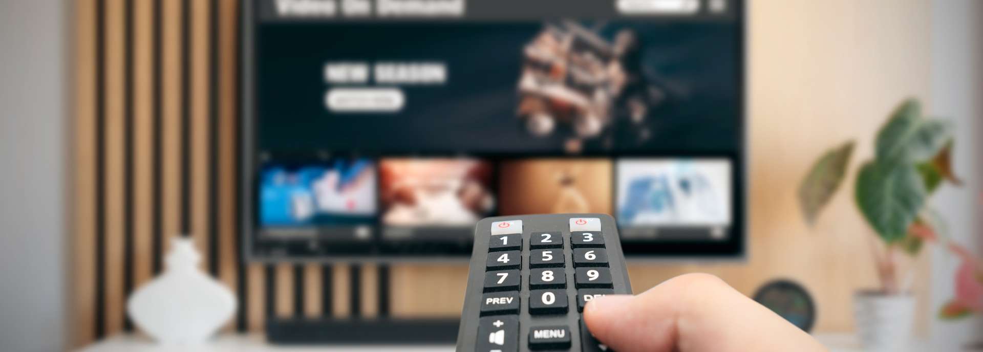 Hand hält eine Fernbedienung vor einem Fernseher mit Streaming-Inhalten auf dem Bildschirm.