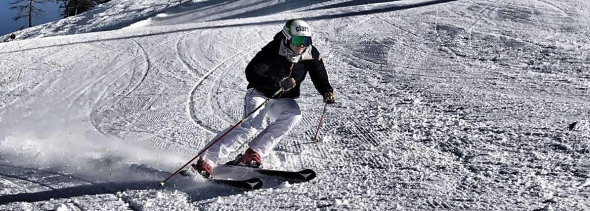 Skirennläuferin fährt auf einer schneebedeckten Piste mit Schwung und konzentriertem Gesichtsausdruck.