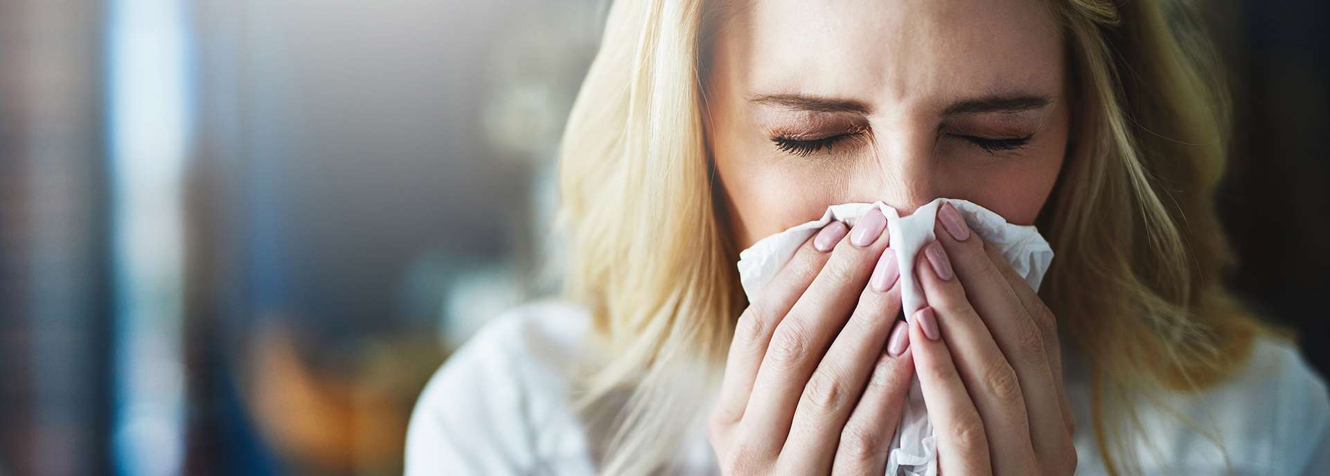 Frau mit geschlossenen Augen hält ein Taschentuch vor ihr Gesicht und wirkt unwohl.