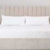 Camera da letto luminosa con letto beige, due cuscini bianchi e materasso su una struttura imbottita.