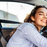 Giovane donna sorride rilassata in auto, mentre si appoggia al volante.