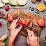 Mani che affettano pomodori freschi su un tagliere di legno, circondati da verdure e spezie.