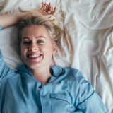 Lächelnde Frau in Schlafanzug liegt entspannt auf einem Bett mit weißen Bettwaren.