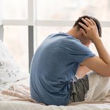 Uomo seduto sul letto, tiene la testa tra le mani, appare pensieroso o stressato.