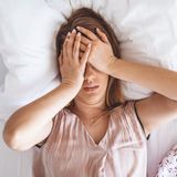 Donna sdraiata a letto con le mani sul viso, appare stressata o inquieta.