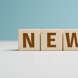 Holzbuchstaben bilden das Wort "NEWS" auf einem hellen Tisch vor einem blauen Hintergrund.