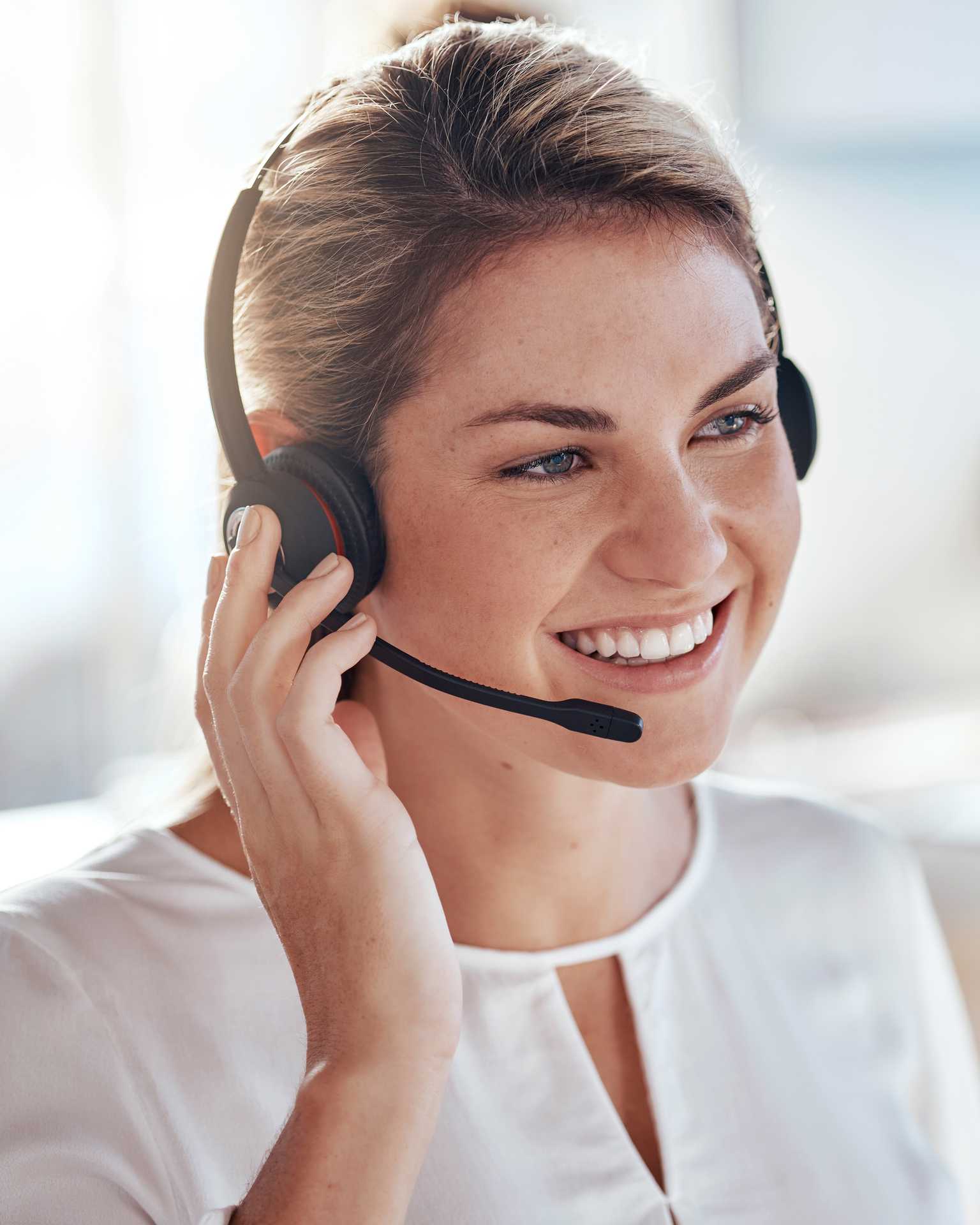 Eine lächelnde Frau mit Headset spricht in ein Mikrofon und schaut freundlich in die Kamera.