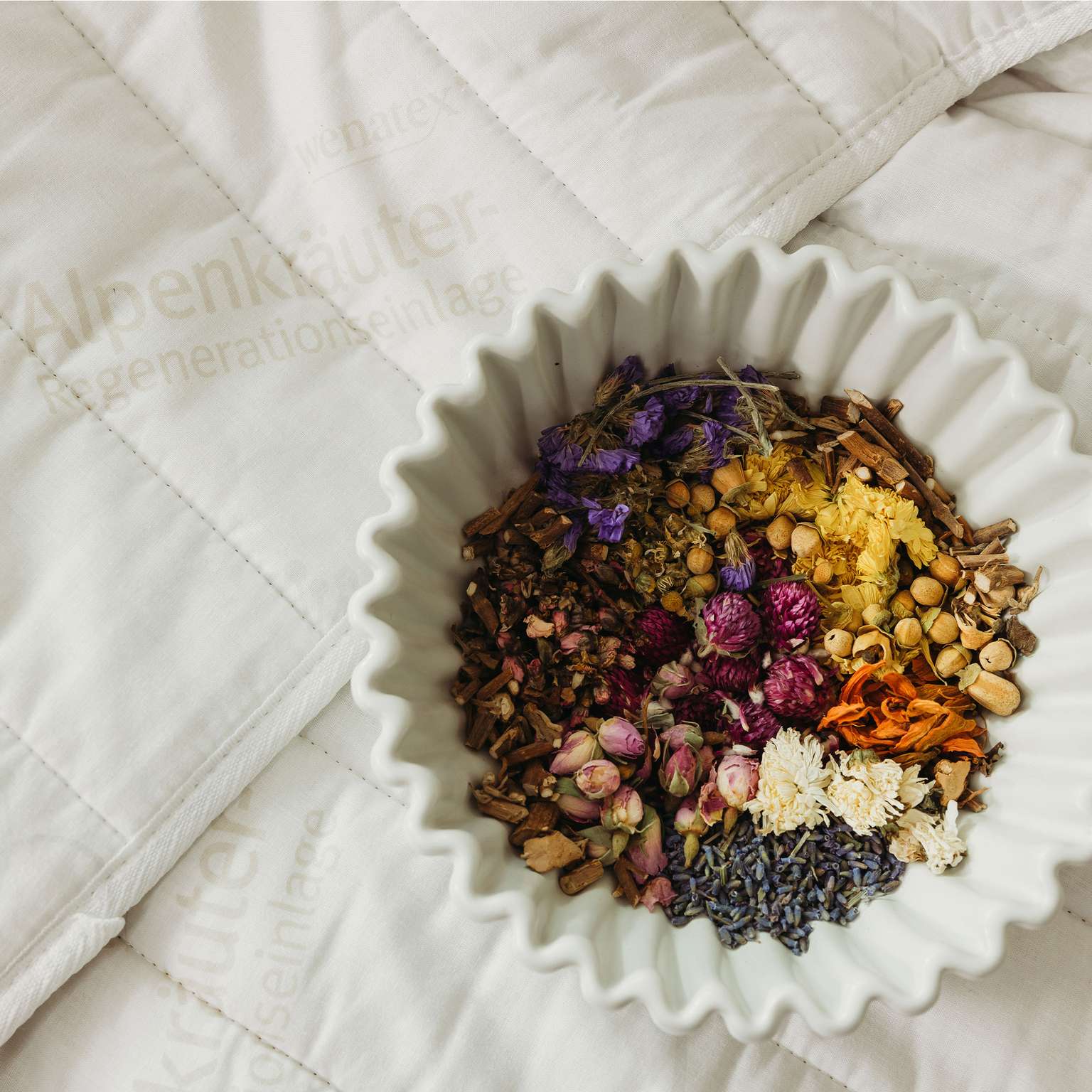 Alpenkräuter-Mischung in einer Schüssel auf einer Bettdecke von Wenatex.