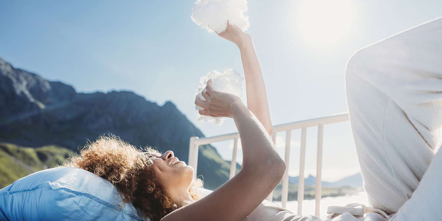 Woman relaxes on a bed with pillows, enjoying the view of nature.