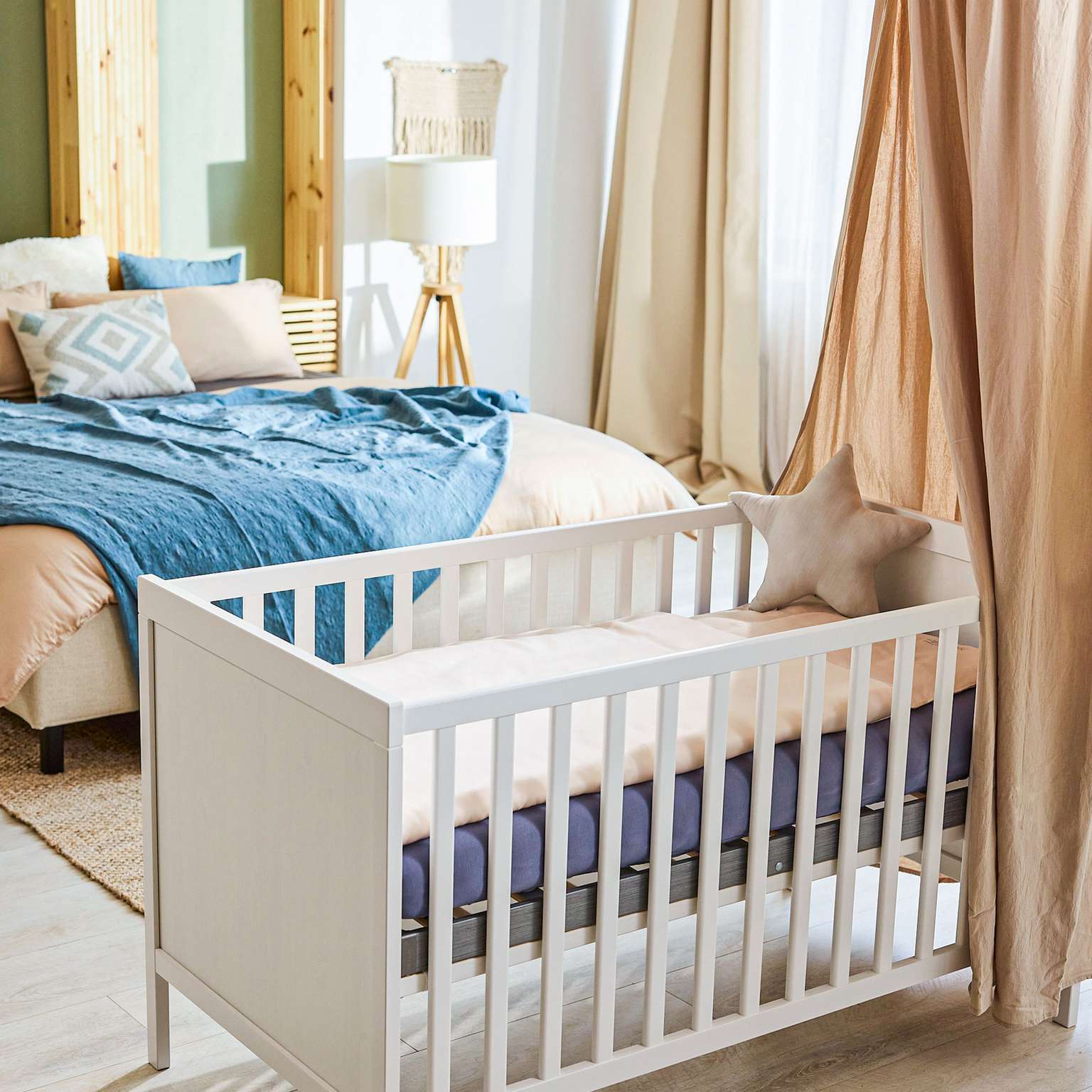 Ein helles Babybett mit einer weichen Matratze in einem stilvollen Schlafzimmer mit Bettwäsche und Dekoration.