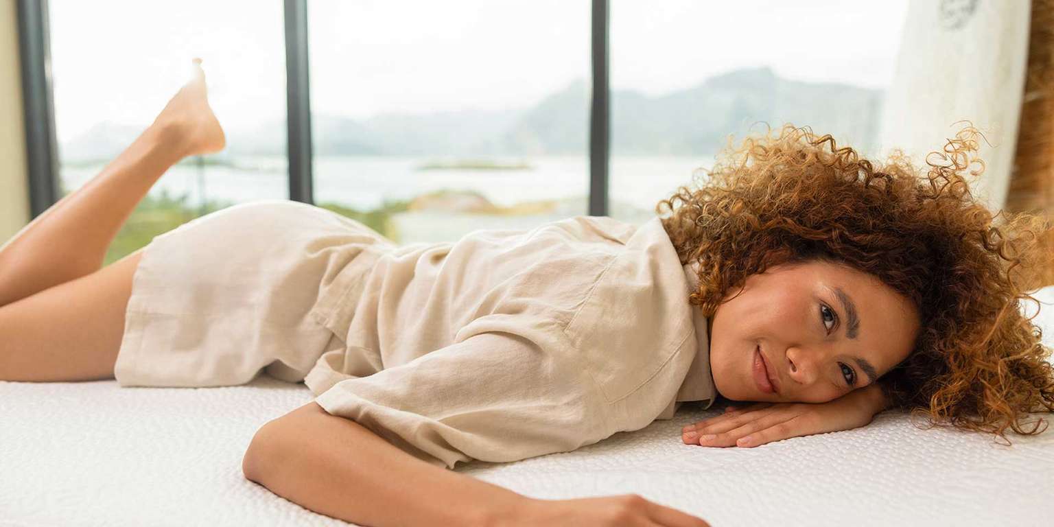 Woman relaxing on a mattress, enjoying the view through a window.