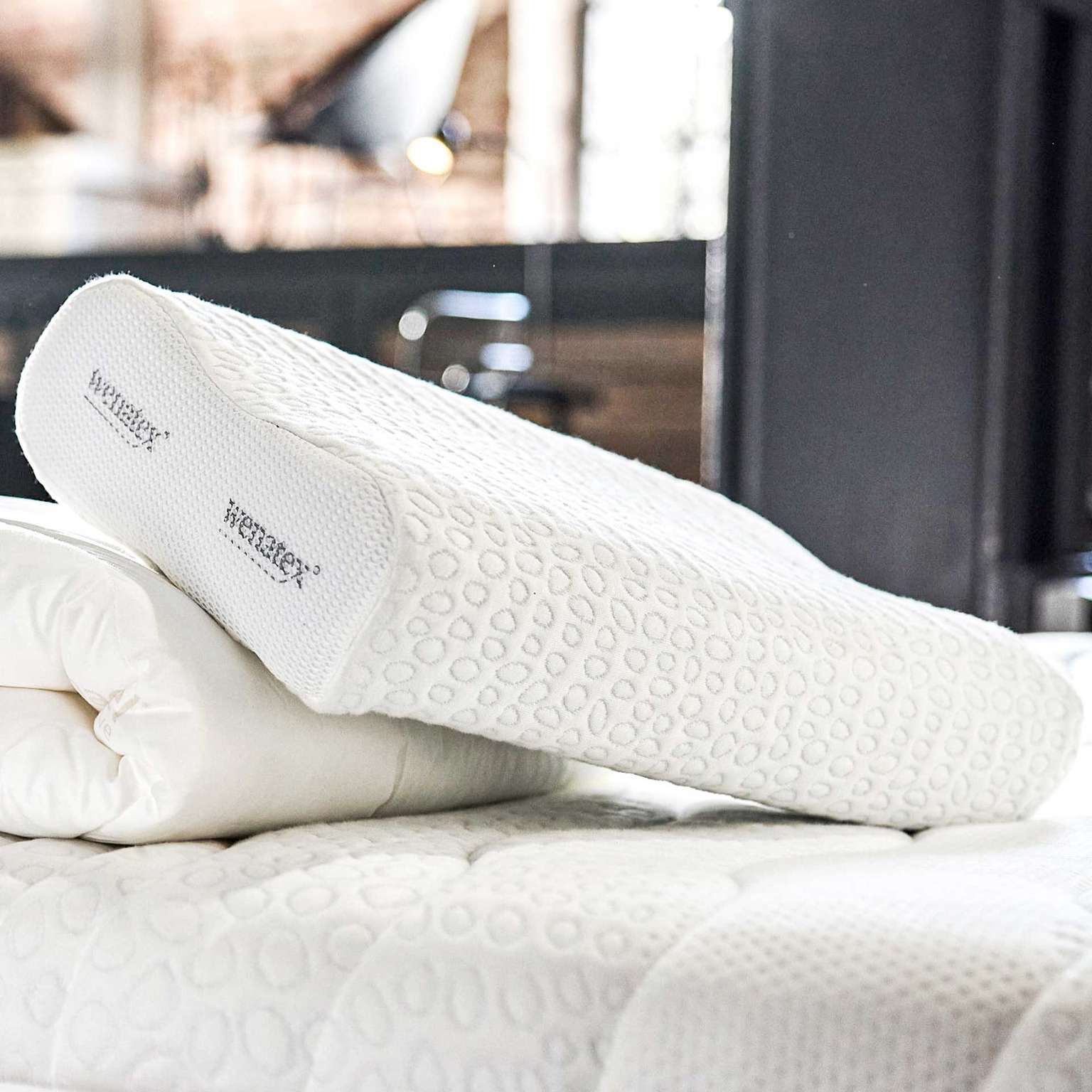 Nackenkissen von Wenatex auf einer Matratze, umgeben von einer Bettdecke.