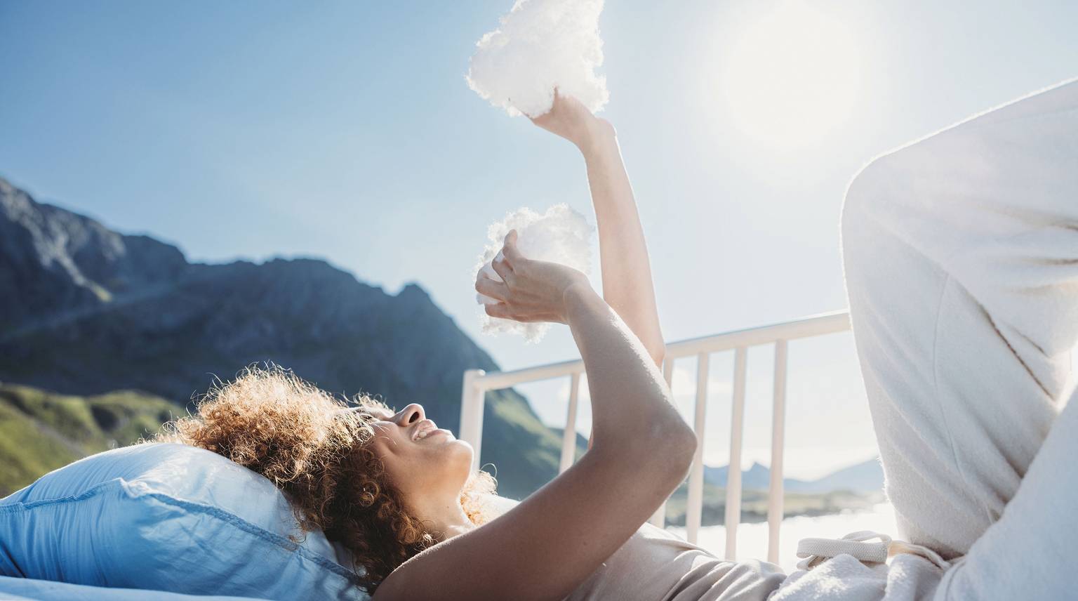 Woman relaxing on an outdoor bed, holding clouds in her hands, surrounded by nature.