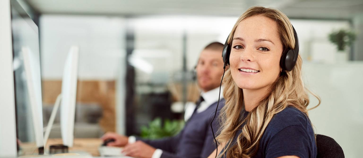 Zwei Büroangestellte mit Headsets arbeiten an Computern in einem modernen Büro.
