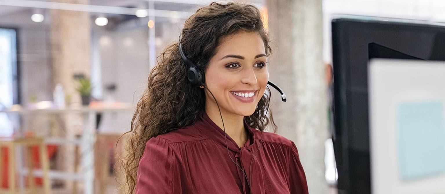 Frau mit Headset lächelt am Schreibtisch vor einem Computer in einem modernen Büro.