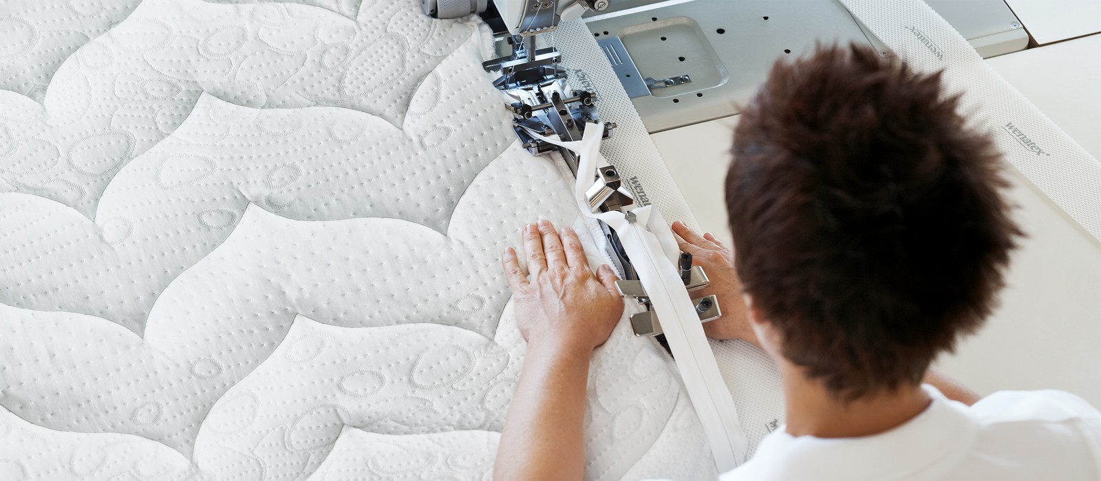 Person näht an einer Matratze mit einer Nähmaschine, die strukturierte Oberfläche ist gut sichtbar.