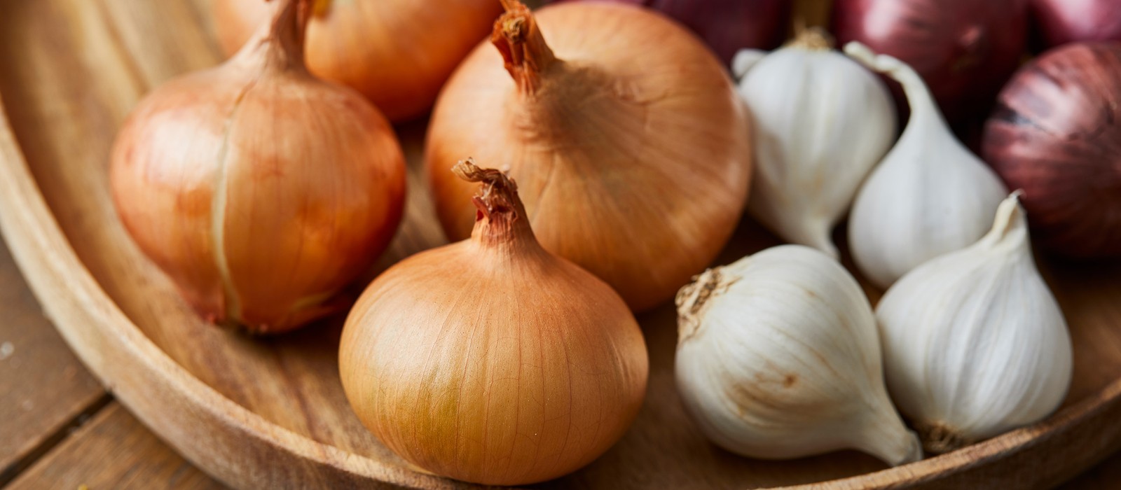 Cipolle e aglio in una ciotola di legno, freschi e colorati disposti con cura.