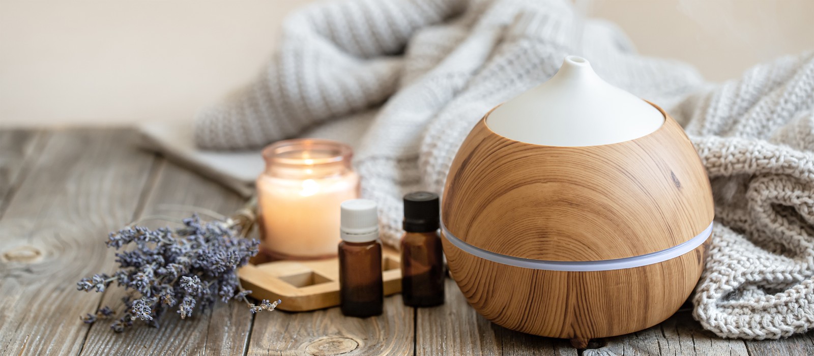 Un diffusore in legno con oli essenziali, una candela e lavanda su un tavolo di legno.