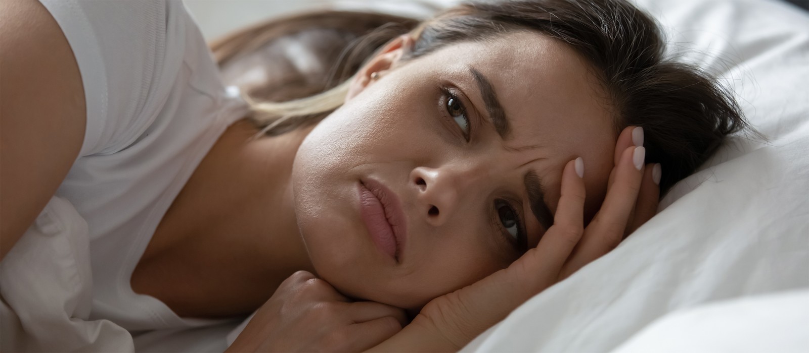 Eine nachdenkliche Frau liegt im Bett und schaut besorgt zur Decke.