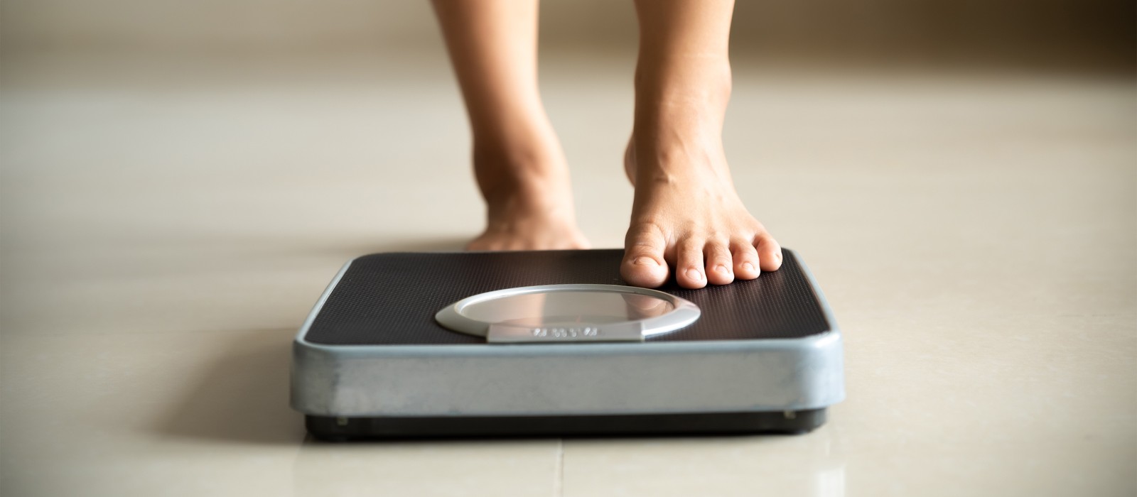 Persona in piedi con un piede su una bilancia digitale su un pavimento chiaro.