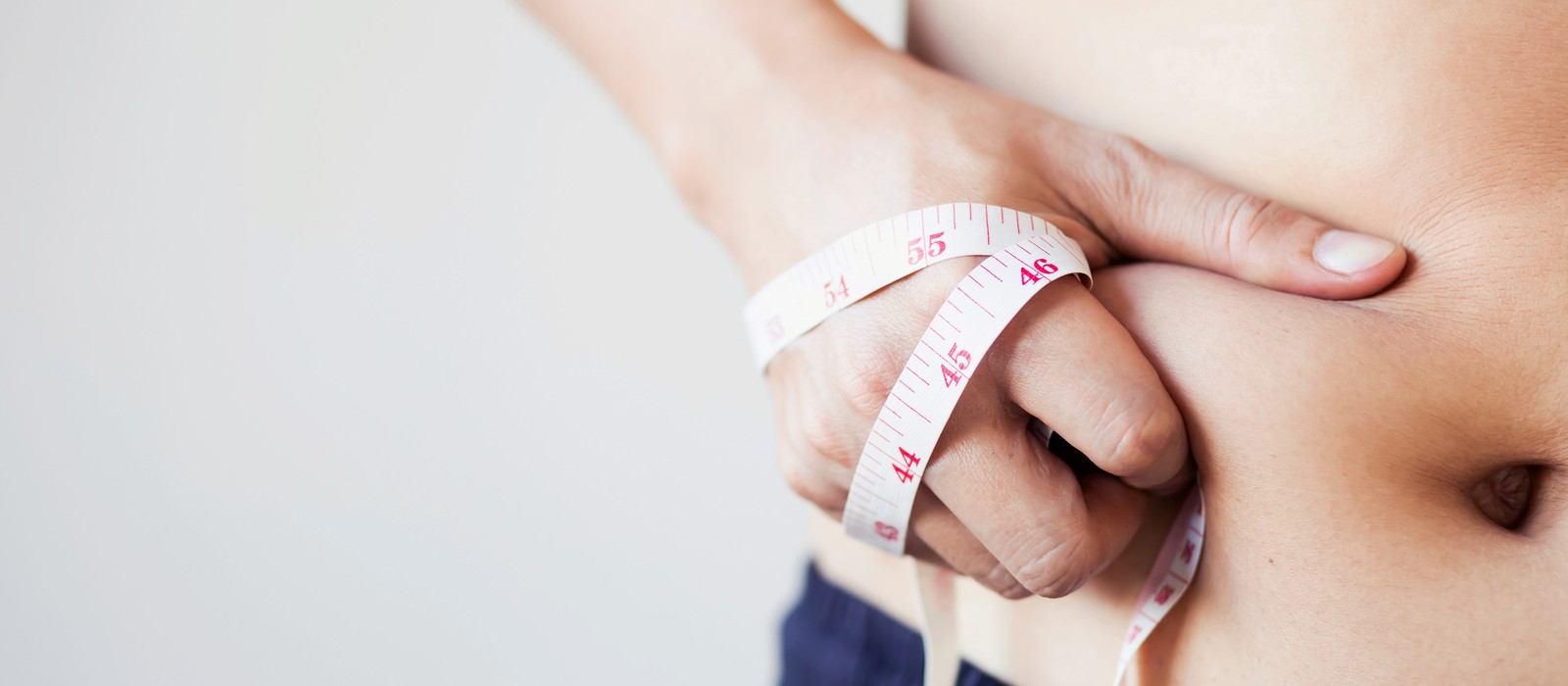 Eine Hand hält ein Maßband um die Taille, das auf eine Körpermessung hinweist.