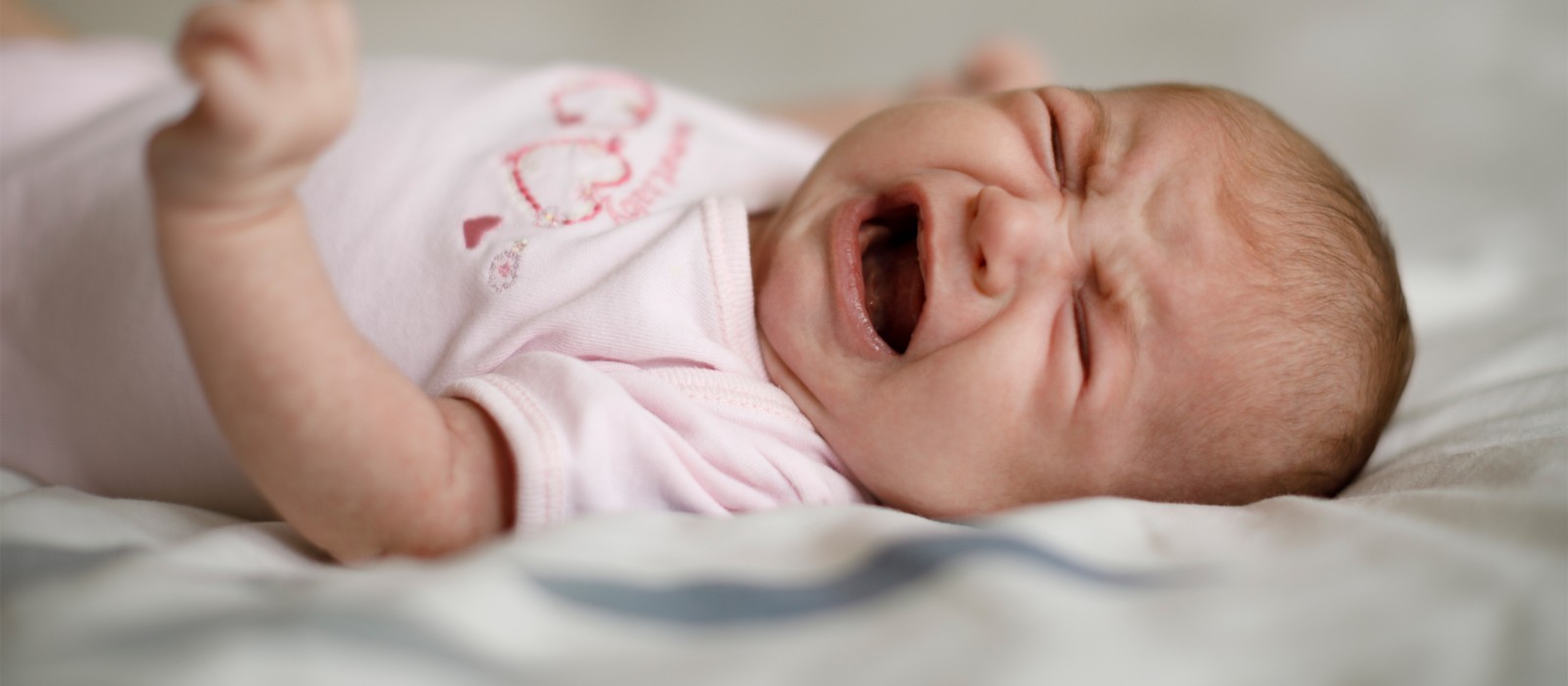 Weinendes Baby auf einem Bett, das sichtbar unruhig und unzufrieden ist.