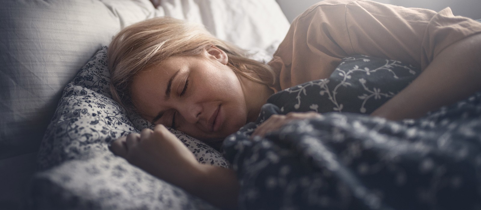 Eine schlafende Frau liegt in einem Bett, umgeben von Kissen und Decken in verschiedenen Mustern.