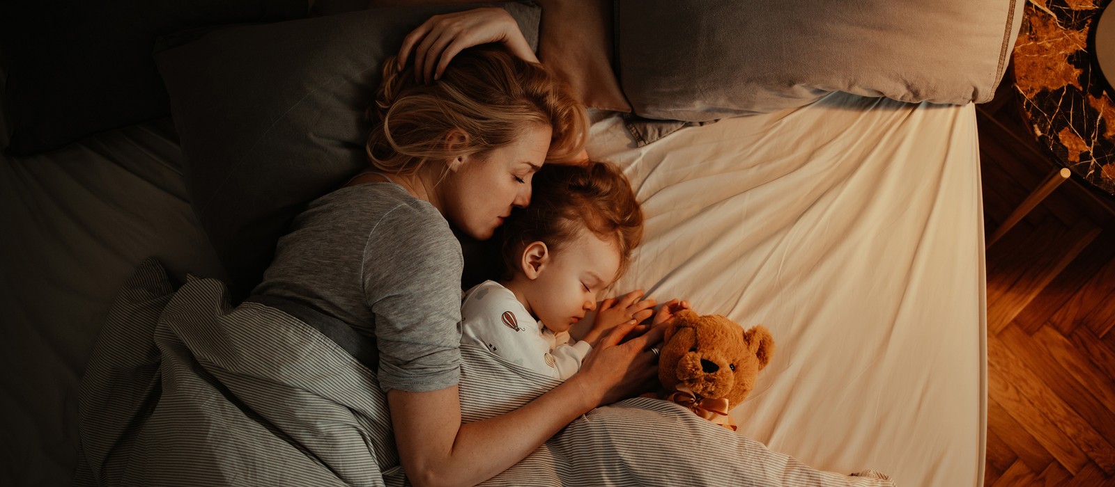 Eine Mutter und ihr Kind schlafen eng umschlungen in einem Bett, umgeben von weichen Kissen und Decken.