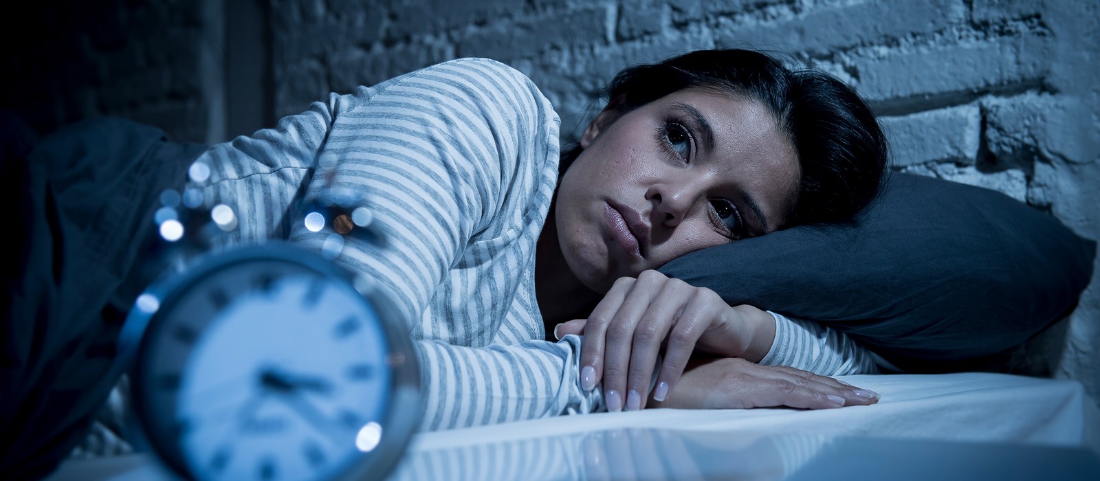 Donna sveglia a letto, guarda pensierosa di lato, la sveglia indica l'ora tarda.