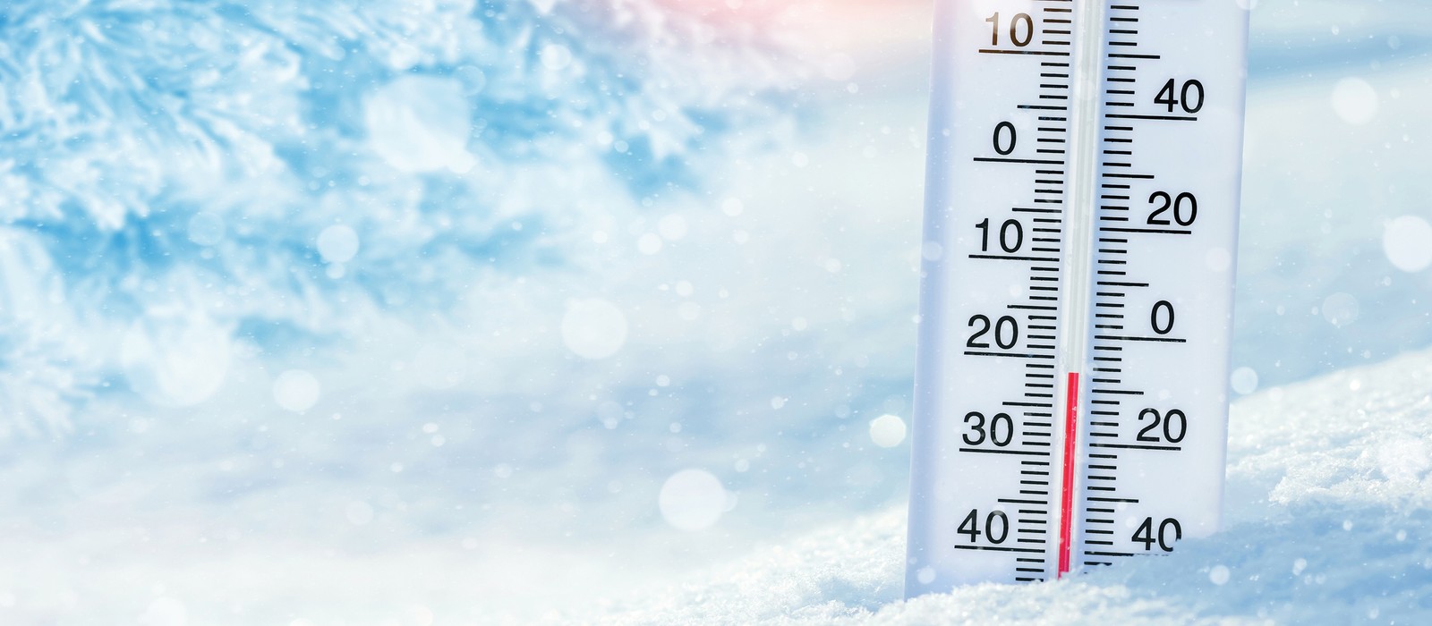 Termometro nella neve, indica basse temperature, con sfondo invernale sfocato.