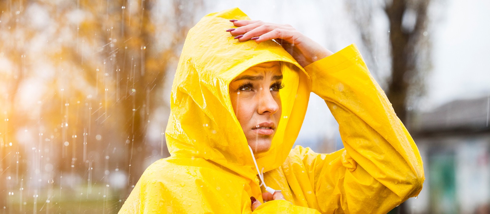 Frau in gelbem Regenmantel steht im Regen und schaut besorgt in die Ferne.
