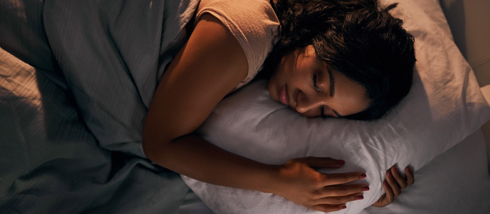 Eine schlafende Person liegt auf einem Kopfkissen, umgeben von Bettwäsche in sanften Farben.