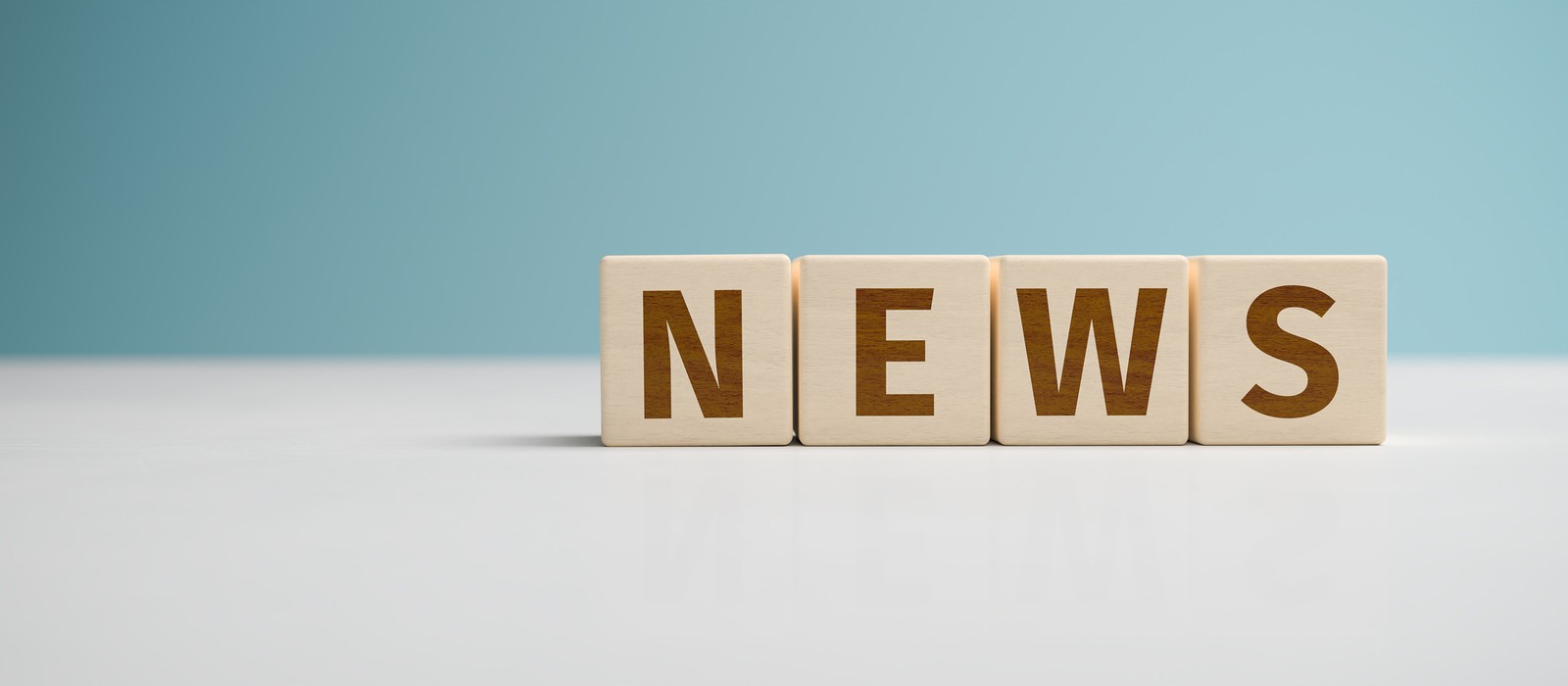 Lettere di legno formano la parola "NEWS" su un tavolo chiaro davanti a uno sfondo blu.
