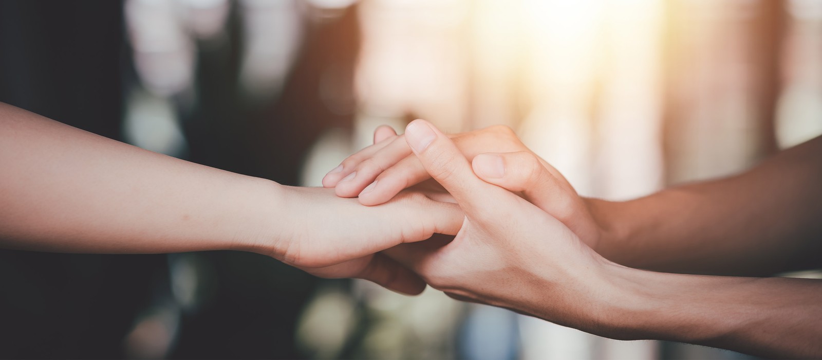 Two hands gently holding each other, symbolizing closeness and support against a warm, blurred background.
