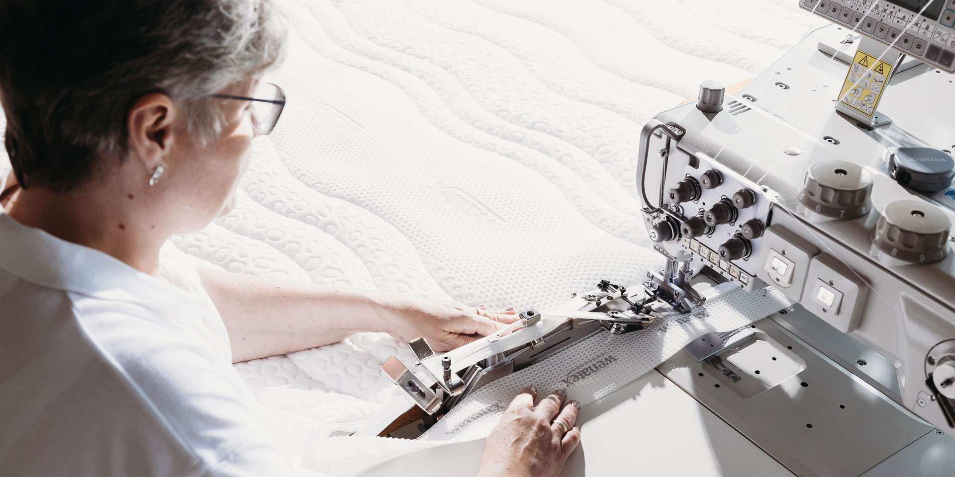 Frau näht einen Matratzenbezug an einer industriellen Nähmaschine auf einem Matratzentextil.