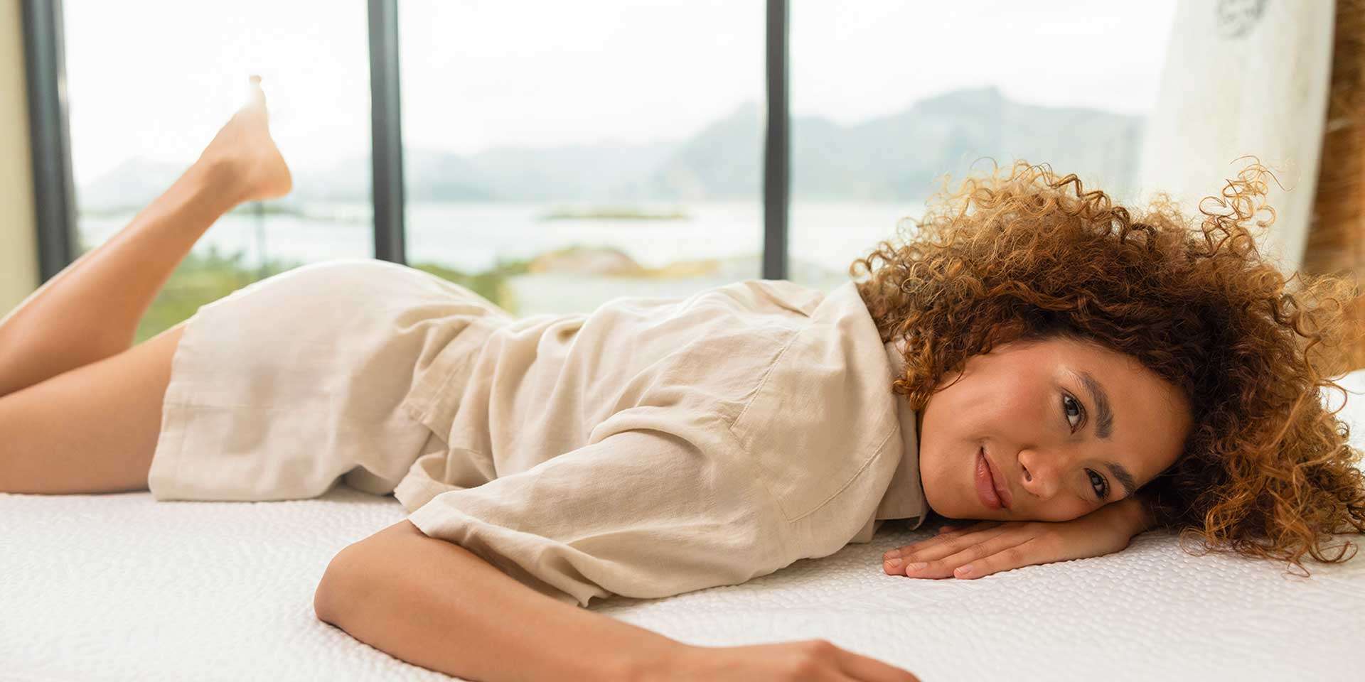 Frau liegt entspannt auf einer Matratze und genießt die Aussicht durch ein Fenster.