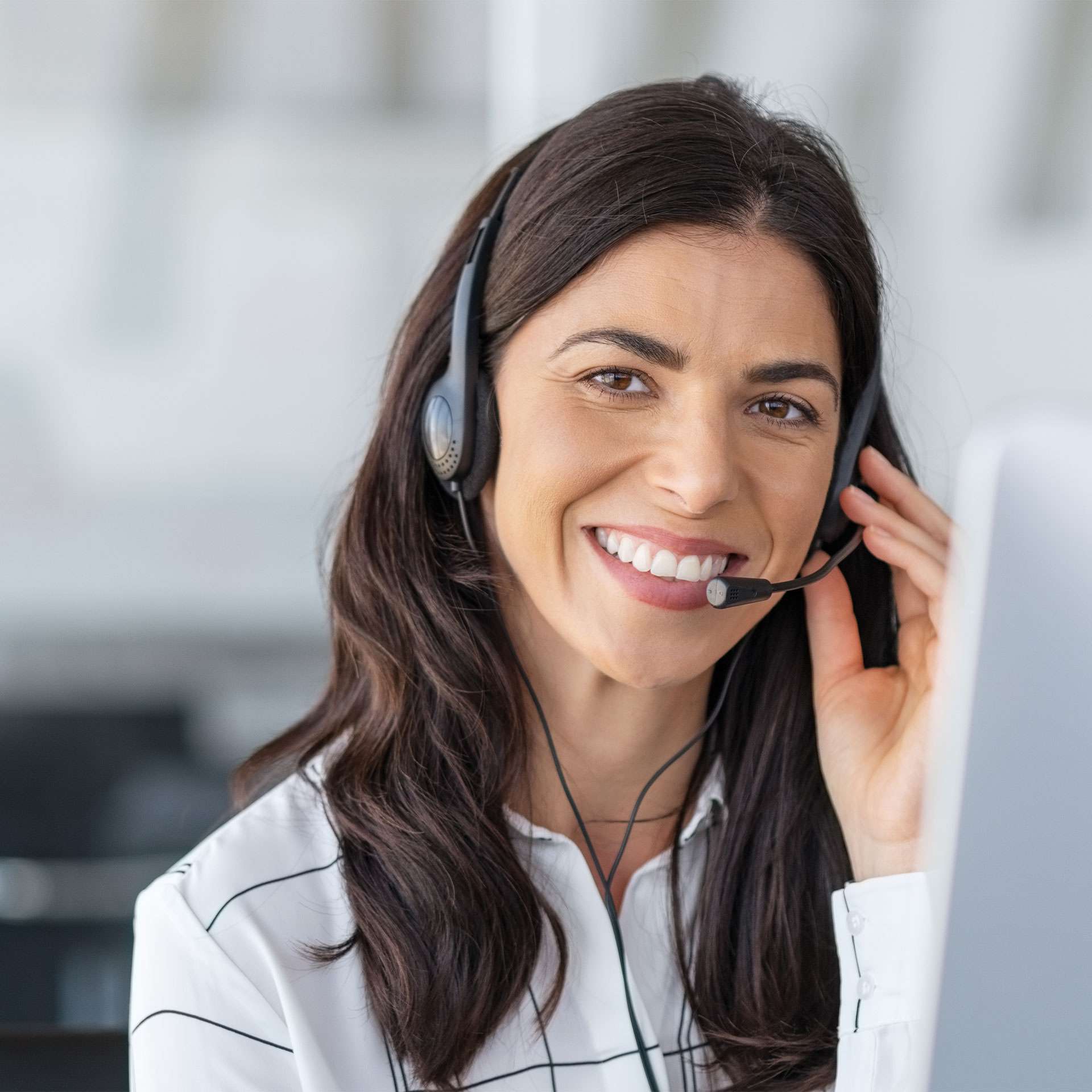Frau mit Headset lächelt freundlich in ein Mikrofon und schaut auf einen Computerbildschirm.