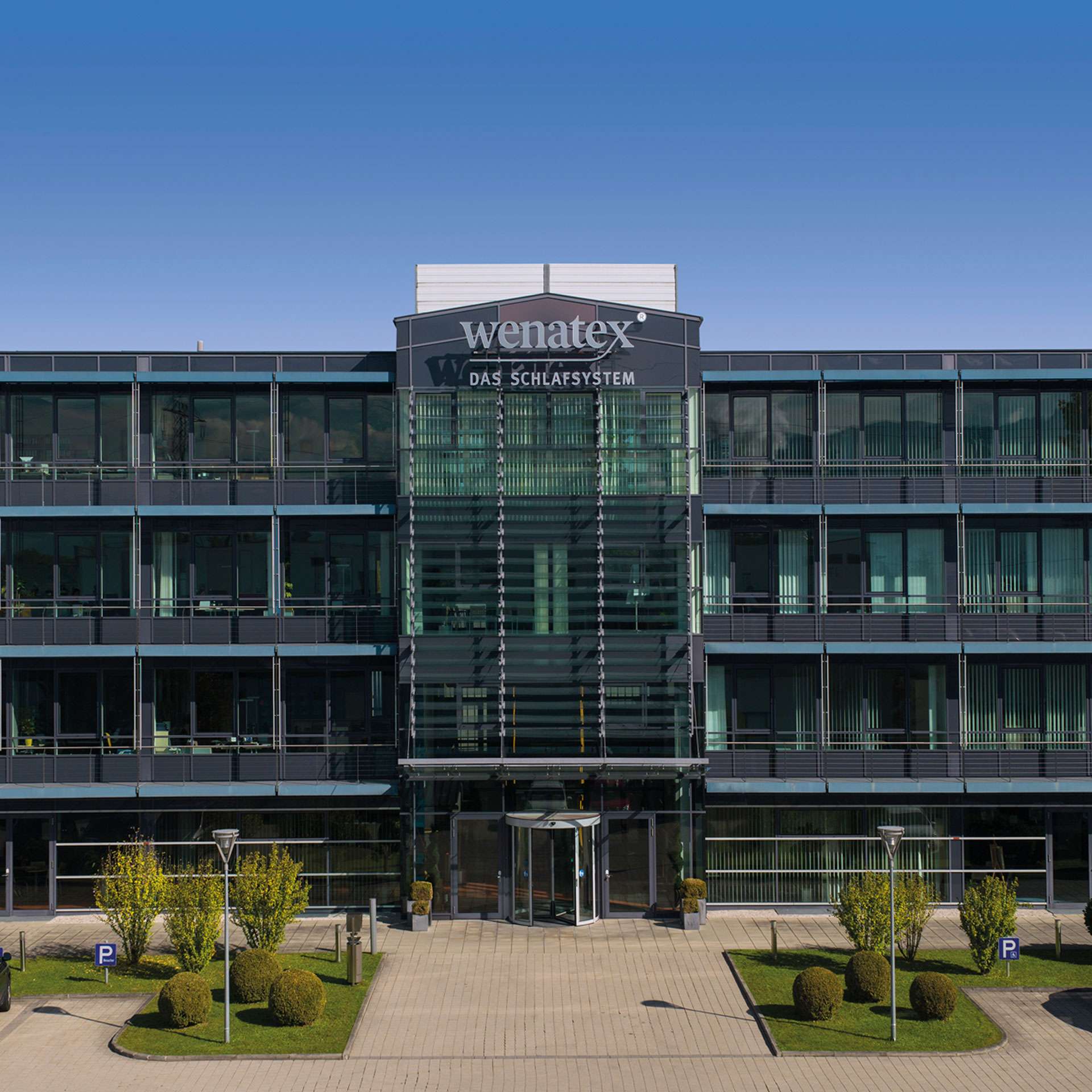 Moderne Bürogebäude mit Glasfassade, umgeben von gepflegten Grünflächen und Parkplätzen.