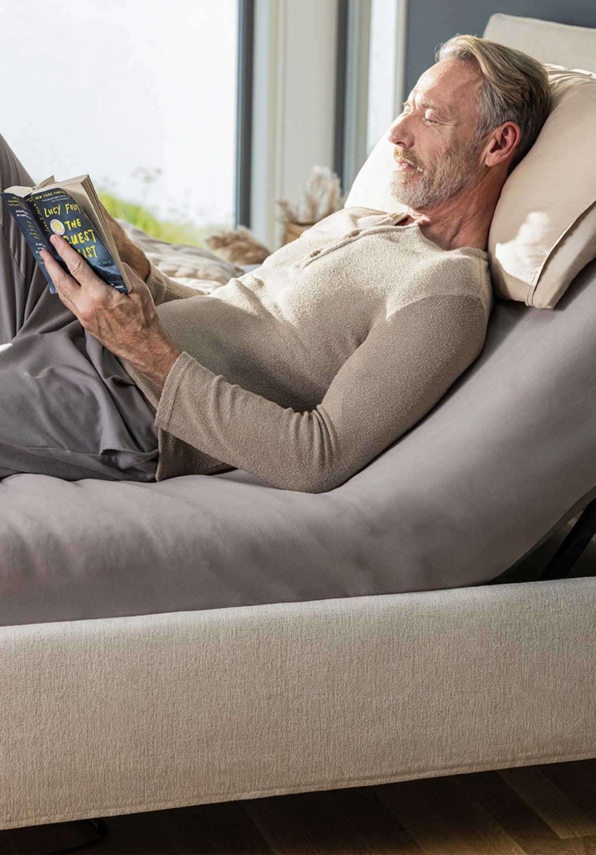 Man relaxes while reading on an adjustable bed with soft bedding and pillows.